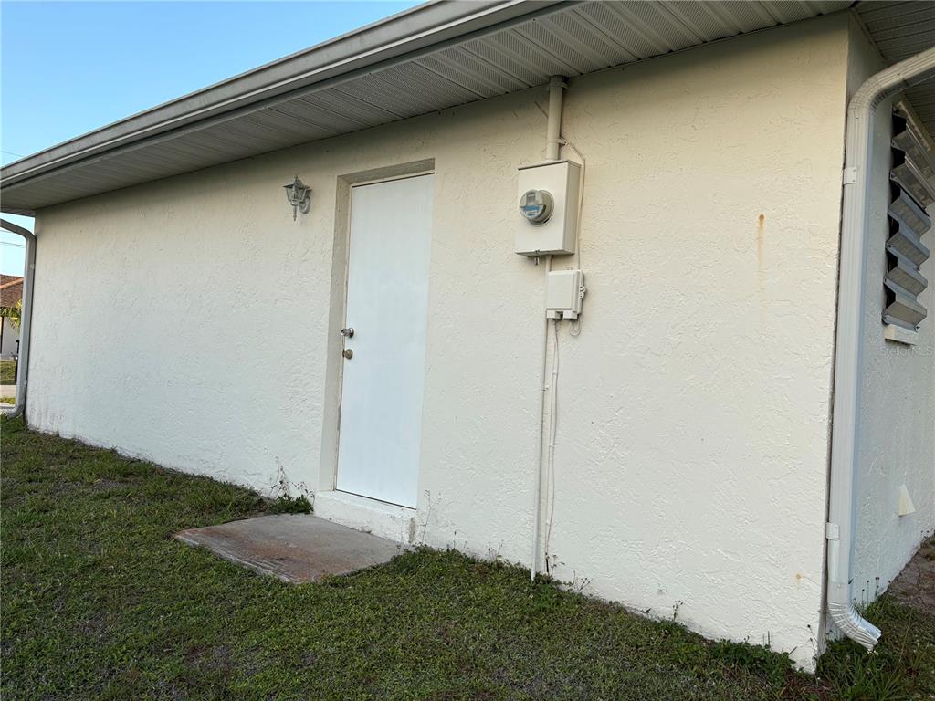 The exterior of a house features a white door, an electrical meter, and a downspout — 18711 KERRVILLE CIRCLE, PORT CHARLOTTE, FL