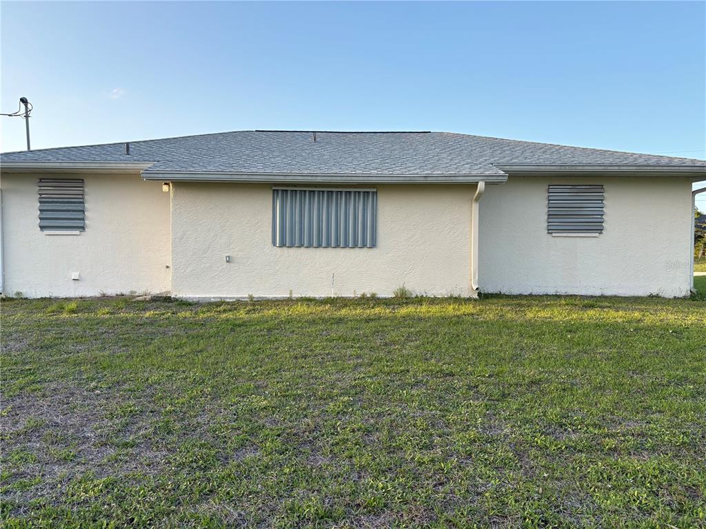 The exterior of a single-story house features light-colored stucco walls and metal hurricane shutters — 18711 KERRVILLE CIRCLE, PORT CHARLOTTE, FL
