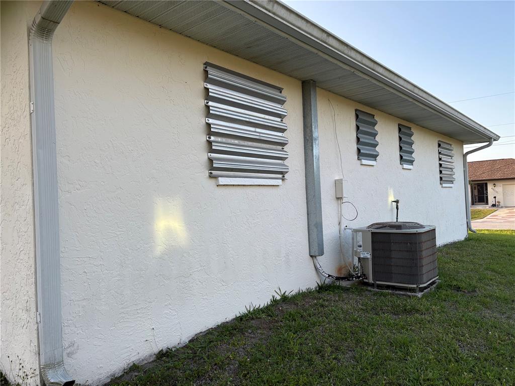 The exterior side of a house features stucco walls, metal hurricane shutters, and an AC unit — 18711 KERRVILLE CIRCLE, PORT CHARLOTTE, FL