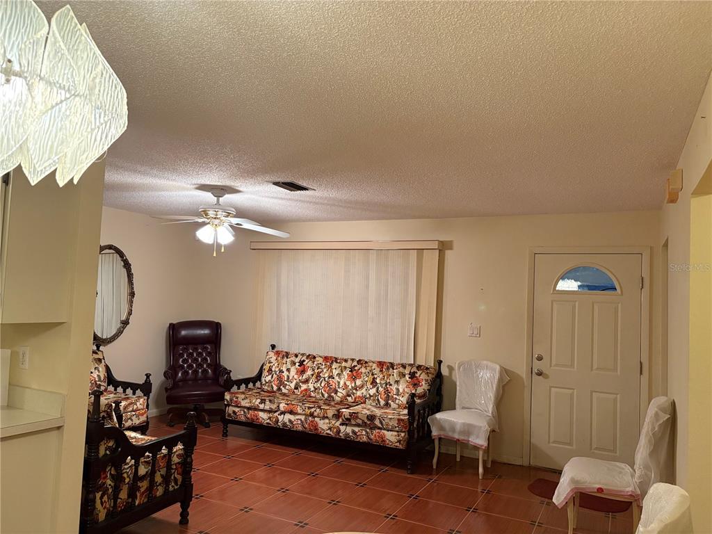 A living room features tiled floors, a floral sofa, a ceiling fan, and a front door — 18711 KERRVILLE CIRCLE, PORT CHARLOTTE, FL