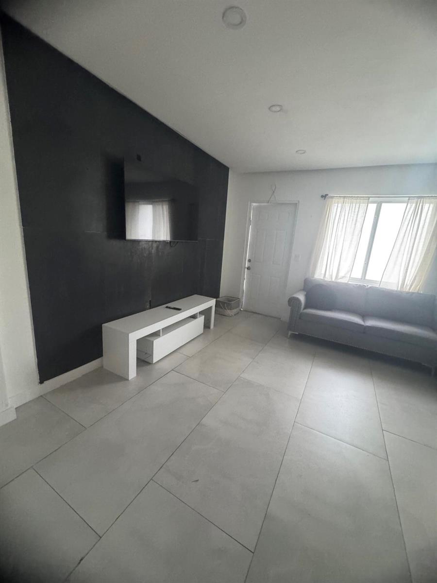 A living room features large light-colored floor tiles, a grey sofa, and a black accent wall — 2201 Greene Street # 2, Hollywood FL 33020, HOLLYWOOD, FL