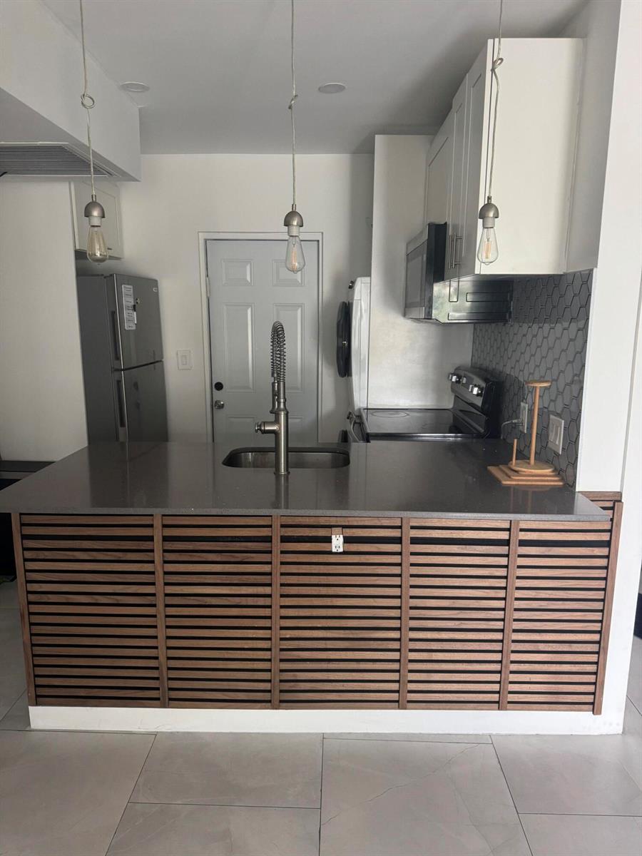 A kitchen features a slatted wood island, gray countertops, white cabinets, and a gray backsplash — 2201 Greene Street # 2, Hollywood FL 33020, HOLLYWOOD, FL