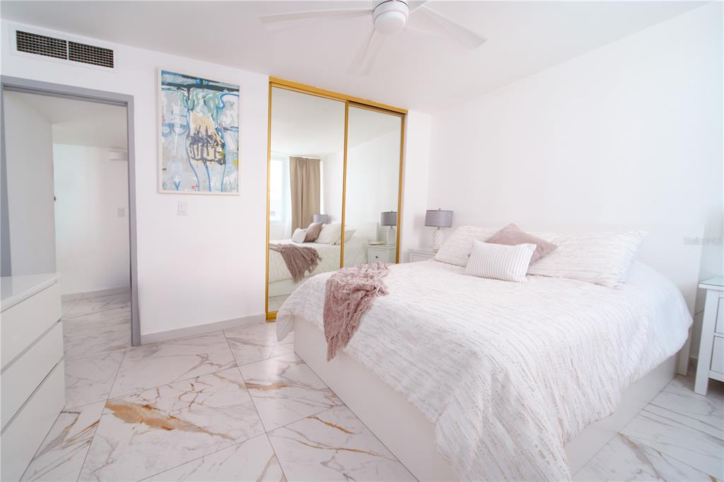 A bedroom features white marble-look tile floors, a bed with white bedding, and mirrored closets — 3409 ISLA VERDE AVENUE UNIT 701, CAROLINA, PR