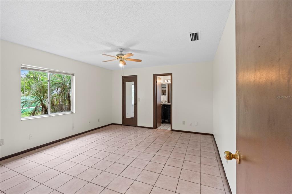 A bedroom with beige tile flooring, a ceiling fan, and a doorway leading to a bathroom — 195 GIBSON WAY, PORT ORANGE, FL