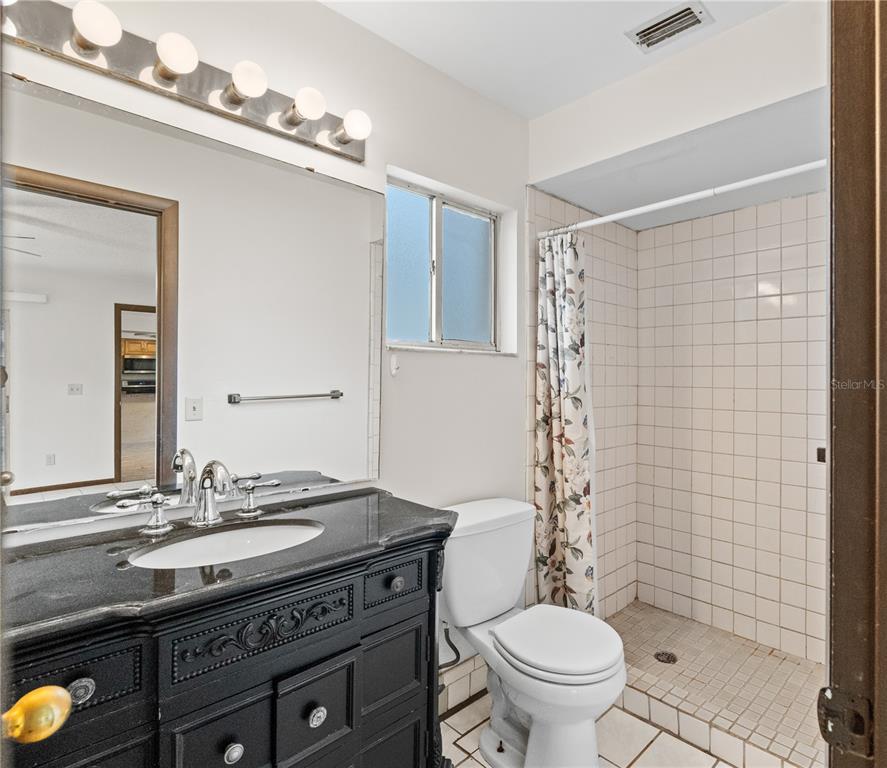 A bathroom features a black vanity with a stone countertop, a toilet, and a tiled shower — 195 GIBSON WAY, PORT ORANGE, FL