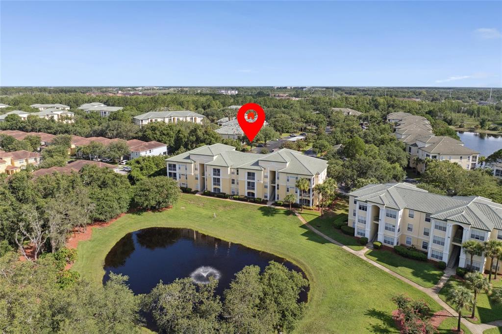 An aerial view shows multi-story apartment buildings surrounding a pond with a fountain — 8816 DUNES COURT UNIT 303, KISSIMMEE, FL