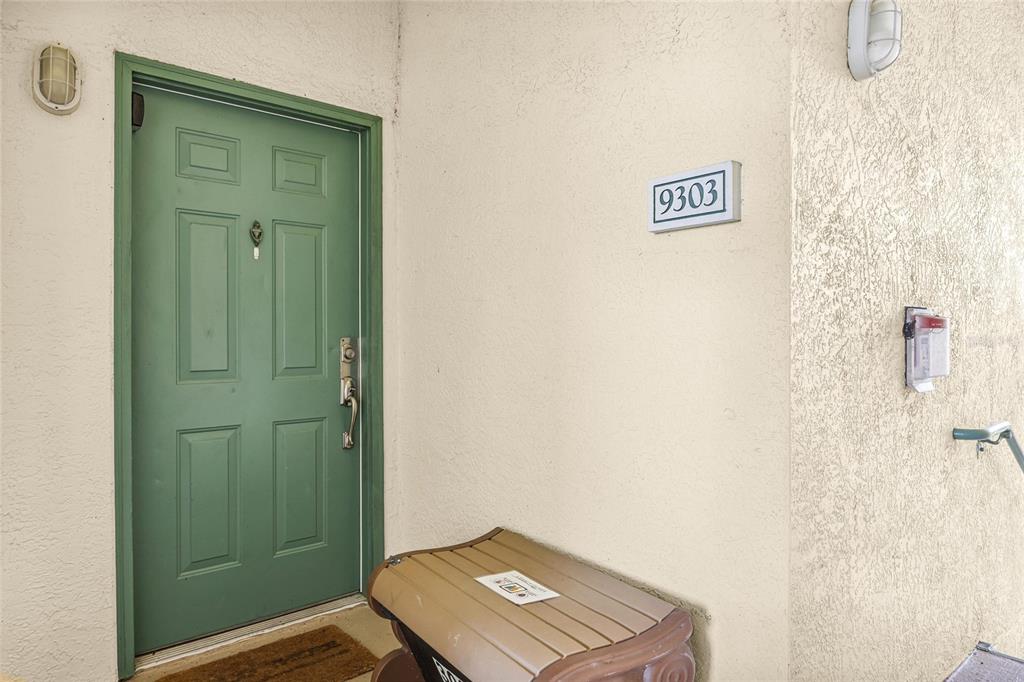 A green front door with a house number sign and a small storage bench outside — 8816 DUNES COURT UNIT 303, KISSIMMEE, FL