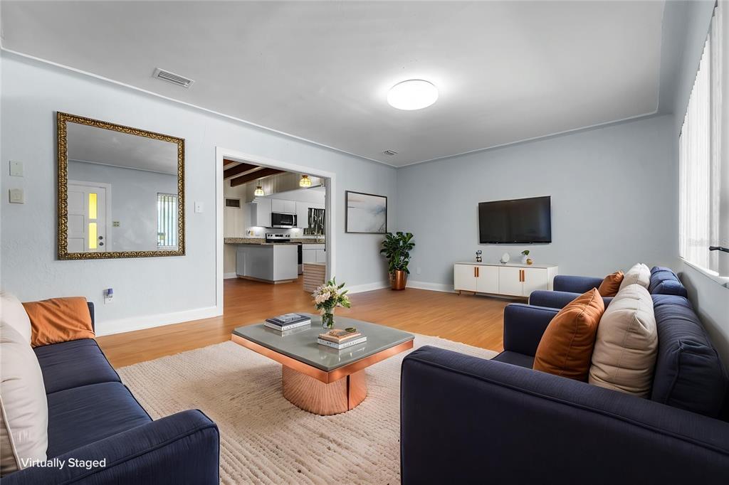 A virtually staged living room features blue sofas, a coffee table, and a kitchen view — 2505 E 19TH AVENUE, TAMPA, FL