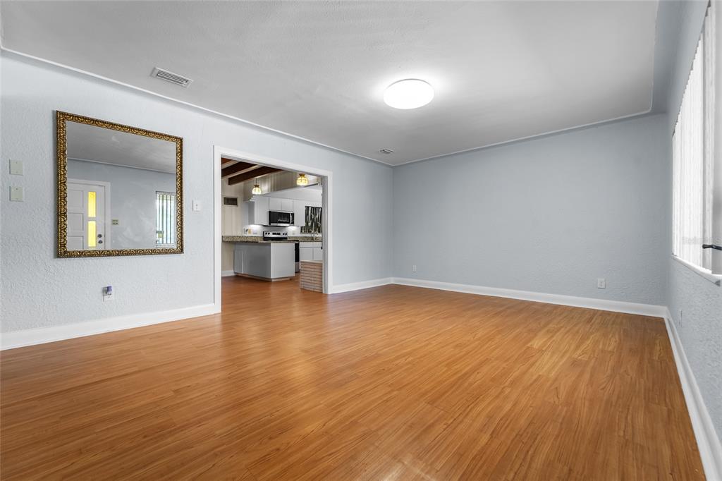 An empty room with light blue walls, wood-look flooring, and a doorway leading to a kitchen — 2505 E 19TH AVENUE, TAMPA, FL