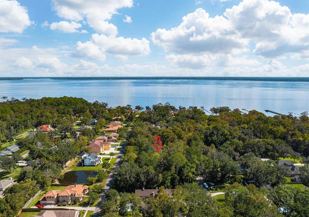 An aerial view shows a wooded residential lot marked with a red arrow near water — RIVERWOOD DRIVE, FLEMING ISLAND, FL