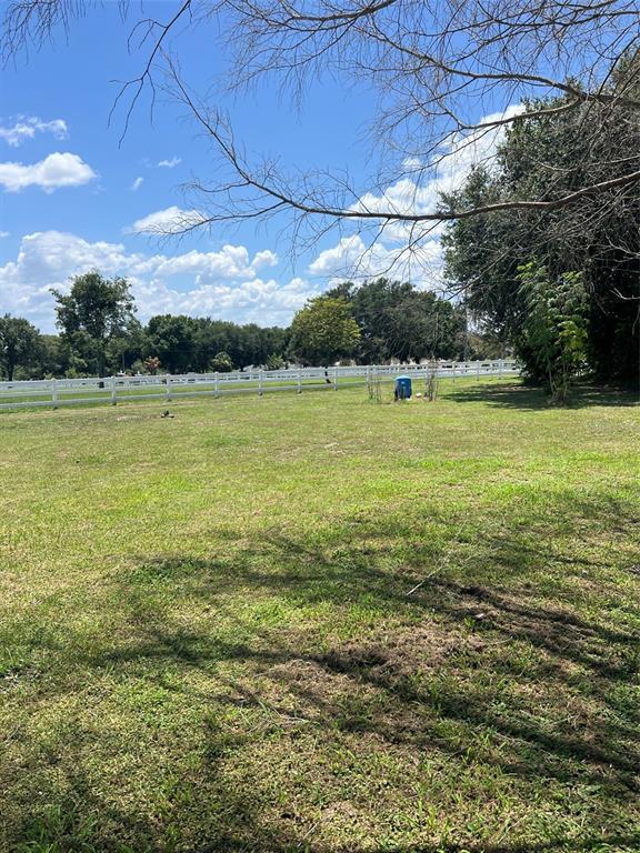 A grassy field features a white fence and a portable toilet under a blue sky — 915 HILLSIDE COURT S, WINTER HAVEN, FL