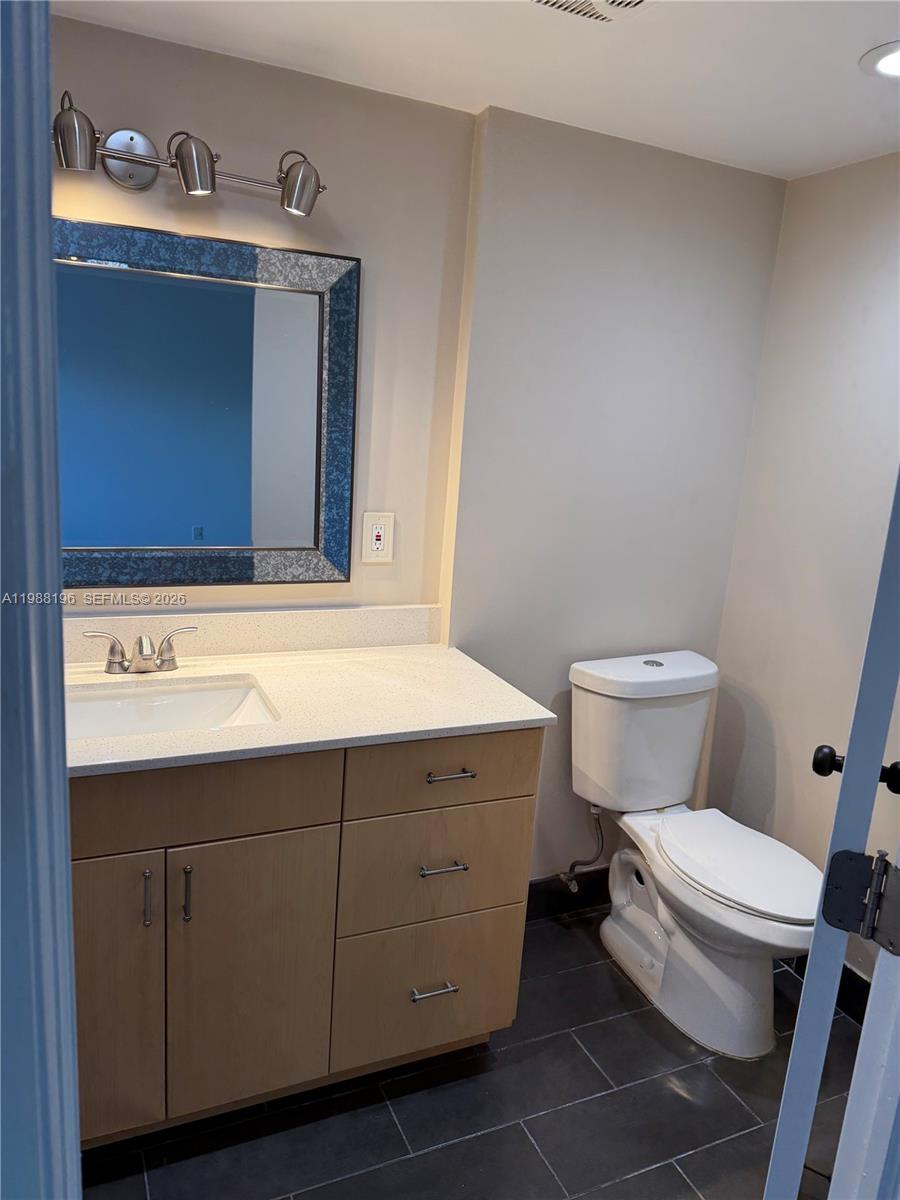 A bathroom features a light wood vanity, white countertop, framed mirror, and dark floor tiles — 9355 SW 8th St # 305, Boca Raton FL 33428, BOCA RATON, FL