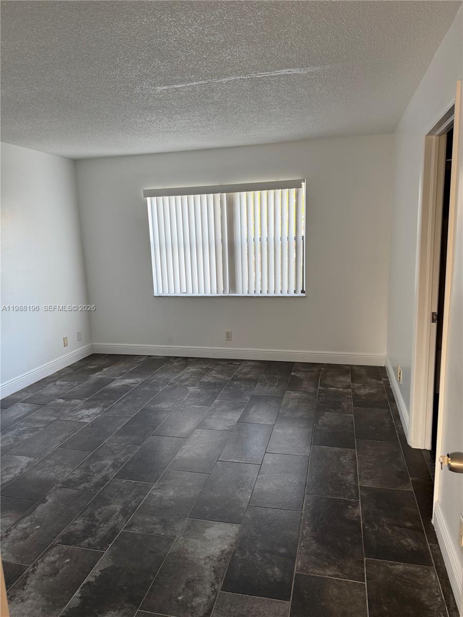 An empty room features white walls, a window with vertical blinds, and dark tile flooring — 9355 SW 8th St # 305, Boca Raton FL 33428, BOCA RATON, FL
