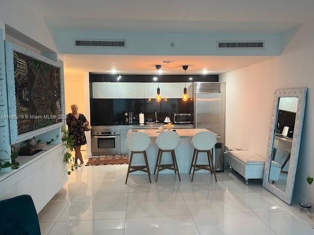 A modern kitchen features white cabinetry, a center island with bar stools, and glossy flooring — 1040 Biscayne Blvd # 2607, Miami FL 33132, MIAMI, FL