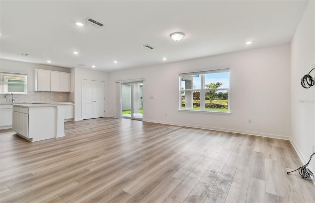 A bright, open-concept living area features light wood-look flooring, a kitchen island, and sliding doors — 10238 CROSS RIVER TRAIL, PARRISH, FL