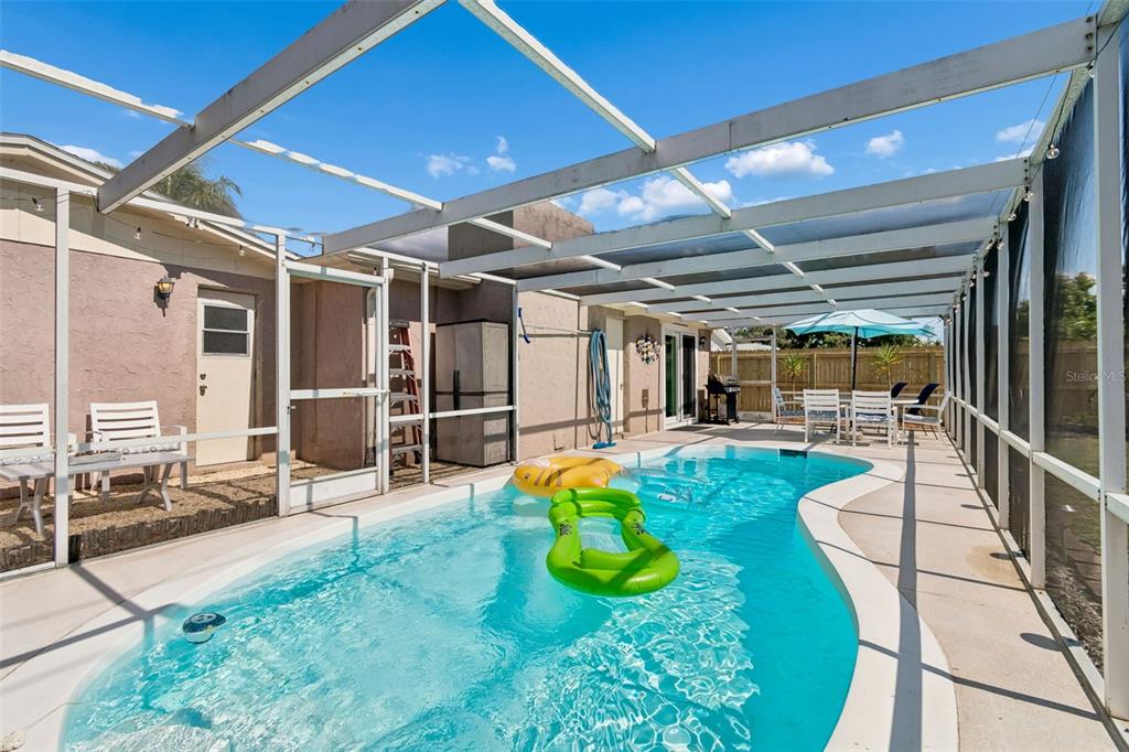 A screened-in patio features a swimming pool with floating rafts and outdoor dining furniture — 1853 DARTMOUTH DRIVE, HOLIDAY, FL