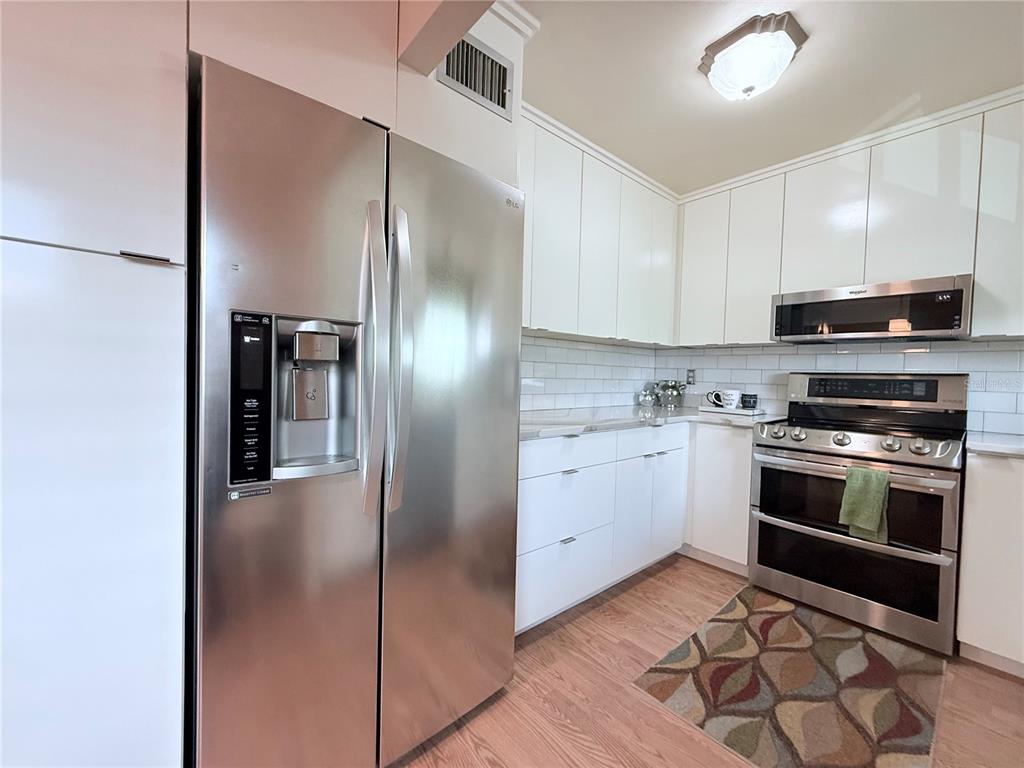 A kitchen features stainless steel appliances, white cabinetry, a subway tile backsplash, and wood flooring — 4460 IRONWOOD CIRCLE UNIT 304A, BRADENTON, FL