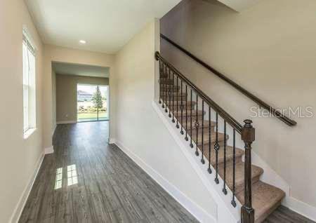A staircase with a dark wood handrail and metal balusters sits beside a hallway — 1391 GREENFIELD LOOP, KISSIMMEE, FL