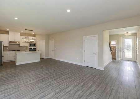 An open-concept kitchen and living area feature light wood-look flooring and white cabinetry — 1391 GREENFIELD LOOP, KISSIMMEE, FL