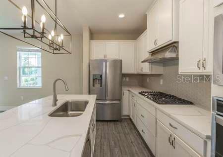 A modern kitchen features white cabinets, a quartz island with a sink, and stainless appliances — 1391 GREENFIELD LOOP, KISSIMMEE, FL