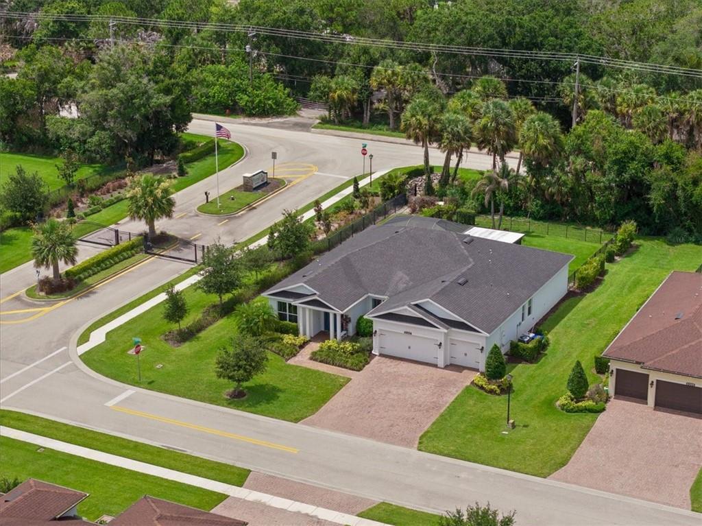 An aerial view shows a single-story house with a gray roof near a gated entrance — VERO BEACH, FL