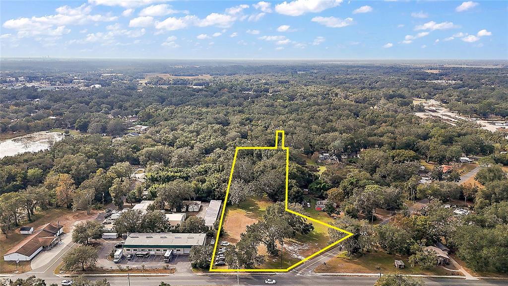 An aerial view shows a vacant, tree-lined lot outlined in yellow near a paved road — 2409 MONTCLAIR ROAD, LEESBURG, FL