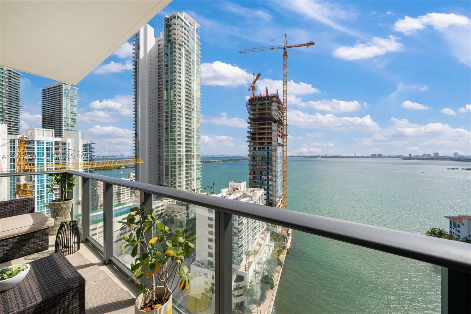 A balcony view overlooks a bay with high-rise buildings and construction cranes under a blue sky — 460 NE 28th St # 1901, Miami FL 33137, MIAMI, FL