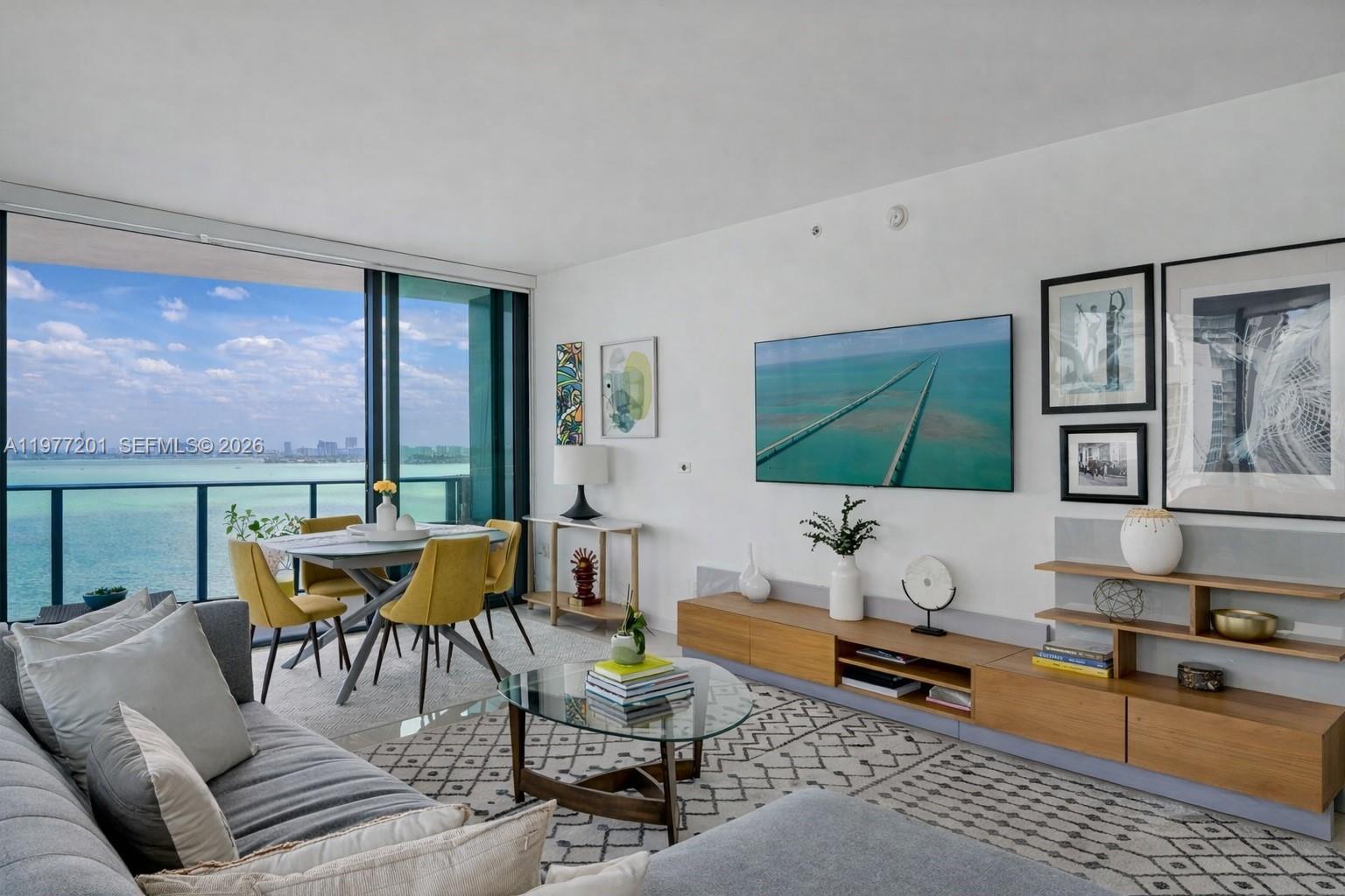 A modern living room features a gray sectional, yellow dining chairs, and a waterfront balcony — 460 NE 28th St # 1901, Miami FL 33137, MIAMI, FL
