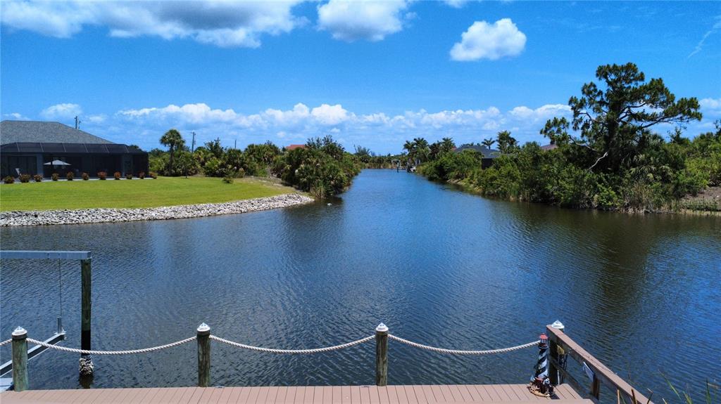 A wooden dock with rope railings overlooks a canal bordered by trees and a house — 10264 WINNIPEG STREET, PORT CHARLOTTE, FL