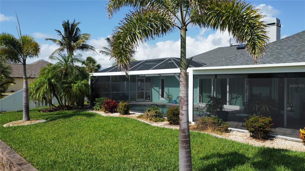 A backyard features a screened-in pool, a grassy lawn, and several palm trees — 10264 WINNIPEG STREET, PORT CHARLOTTE, FL