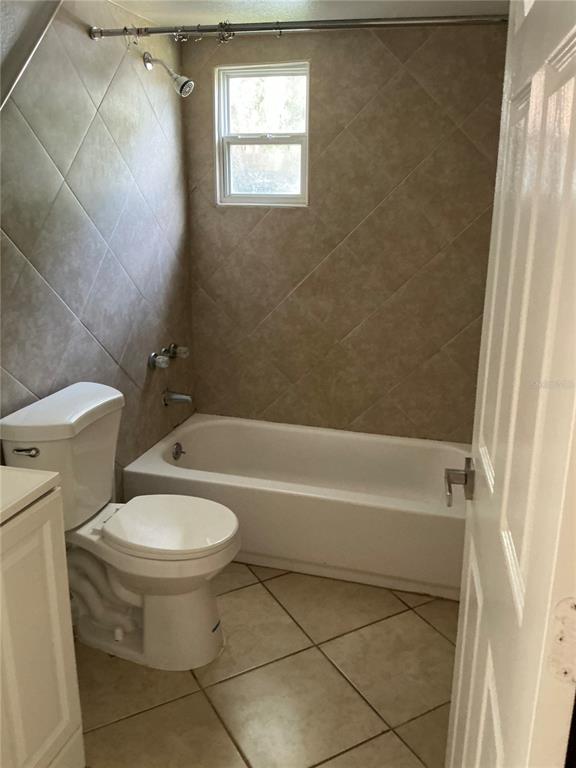 A bathroom features a white toilet, a bathtub with a showerhead, and beige tiled walls — 3495 FOREST DRIVE, KISSIMMEE, FL