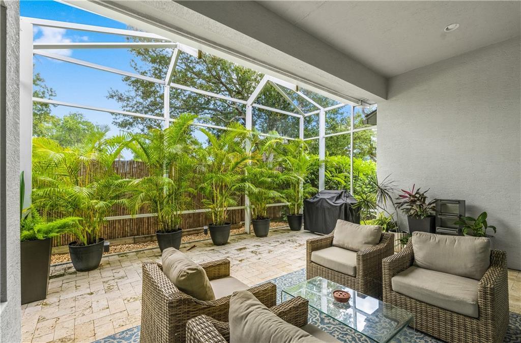 A screened-in patio features stone pavers, wicker furniture, and potted palm trees — VERO BEACH, FL