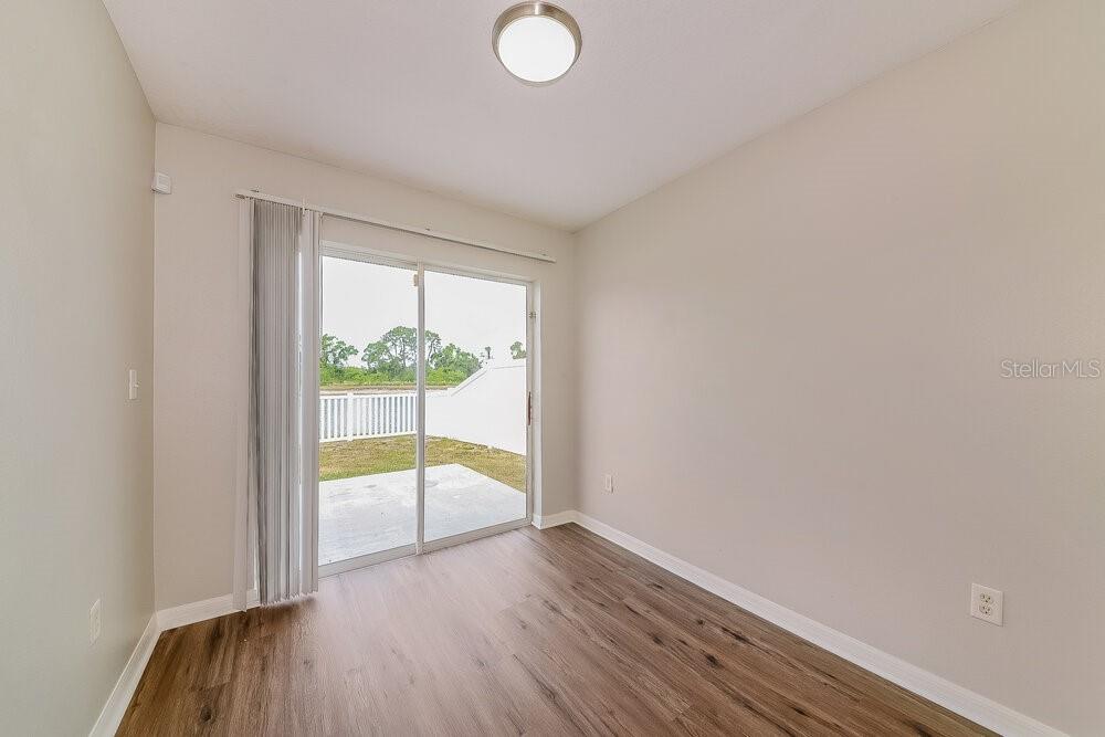 An empty room with wood-look flooring, beige walls, and a sliding glass door to a patio — 727 CRISTELLE JEAN DRIVE, RUSKIN, FL