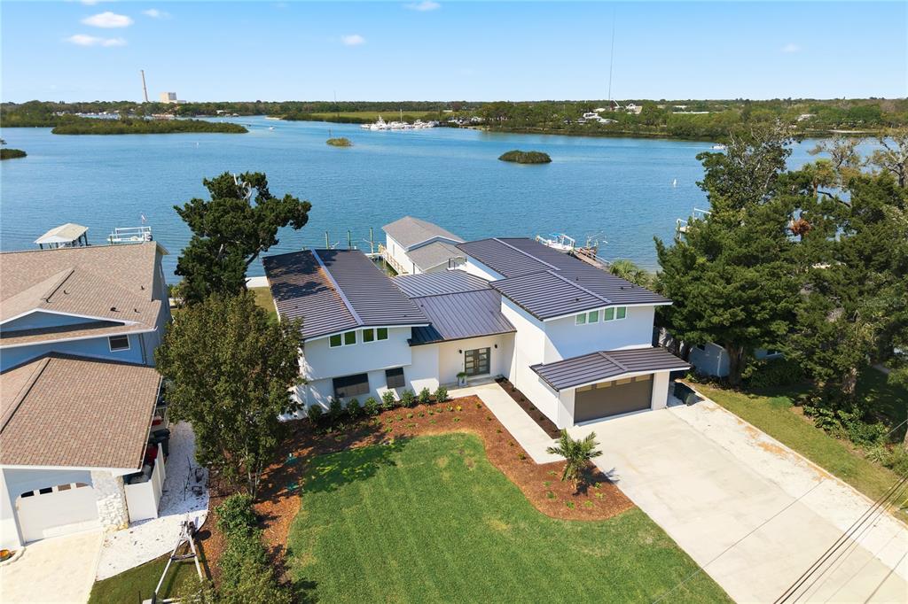 An aerial view shows a modern white house with a dark metal roof near water — 915 BAYSHORE DRIVE, TARPON SPRINGS, FL