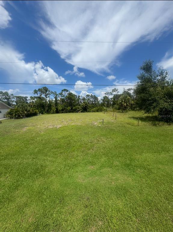 A grassy, vacant residential lot features scattered wooden survey stakes under a blue sky — 6657 GASPARILLA PINES BOULEVARD, ENGLEWOOD, FL