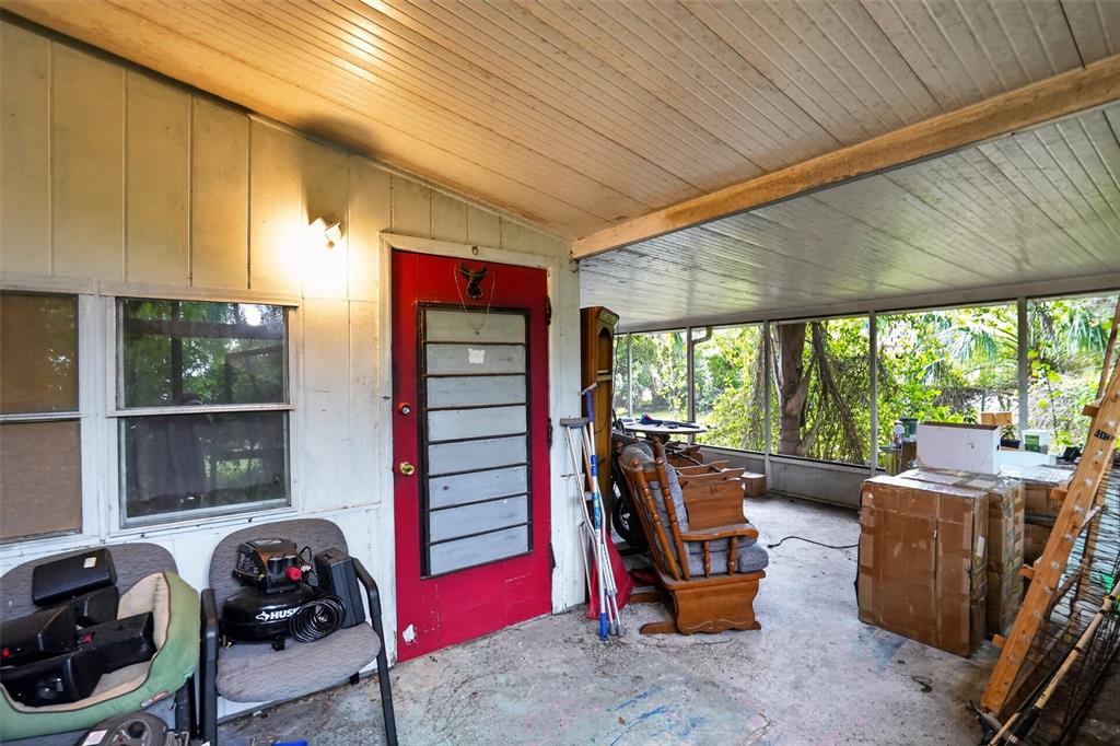 A covered porch features a red door, a concrete floor, and various items of furniture — 509 DOMINO DRIVE N, RUSKIN, FL