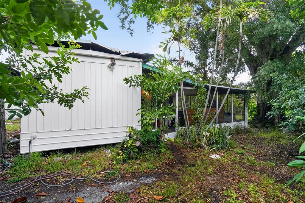 A white mobile home exterior features a screened-in porch surrounded by trees and overgrown landscaping — 509 DOMINO DRIVE N, RUSKIN, FL