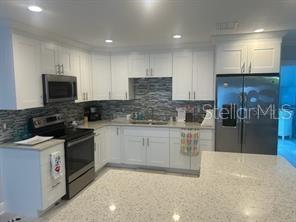 A kitchen features white cabinetry, stainless steel appliances, and a light-colored quartz countertop — 196 OVERBROOK DRIVE E, LARGO, FL