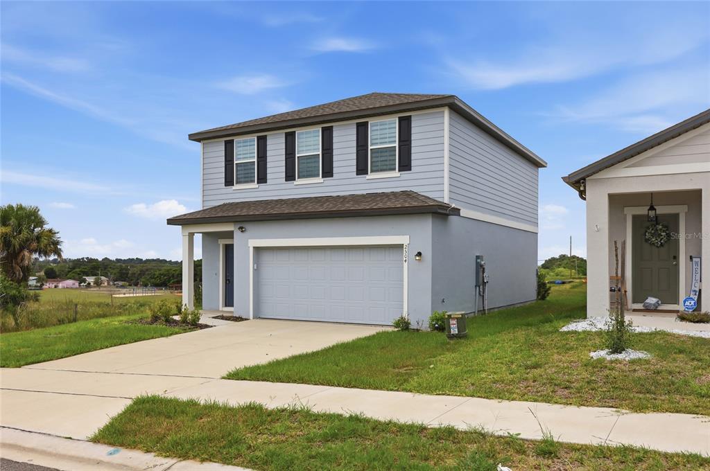 A two-story house with light blue siding, a gray garage door, and a concrete driveway — 2504 PEONY PL, LAKE HAMILTON, FL