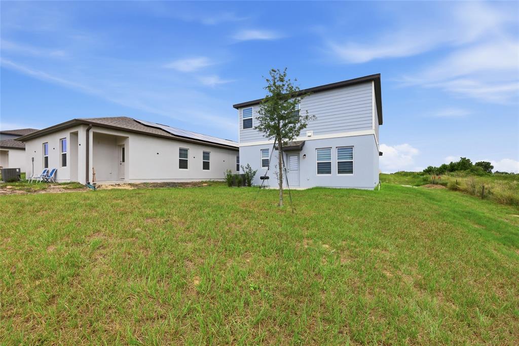 The rear exterior of two adjacent suburban houses features light-colored siding and a grassy yard — 2504 PEONY PL, LAKE HAMILTON, FL