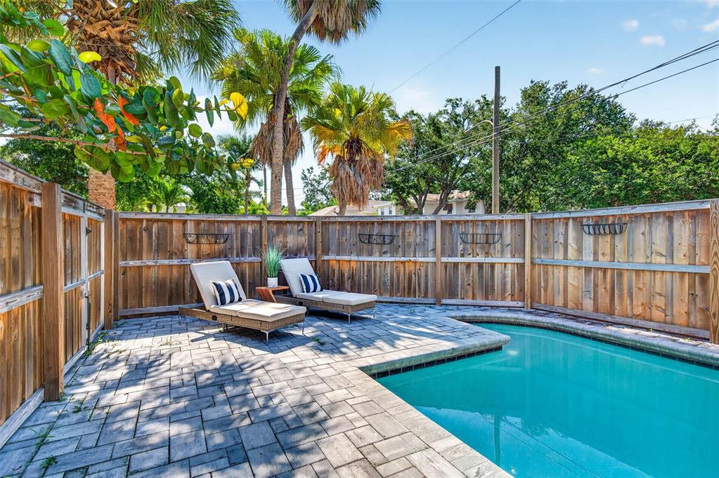 A backyard patio features two lounge chairs beside a swimming pool enclosed by a wooden fence — 1330 CHERRY STREET NE, ST PETERSBURG, FL