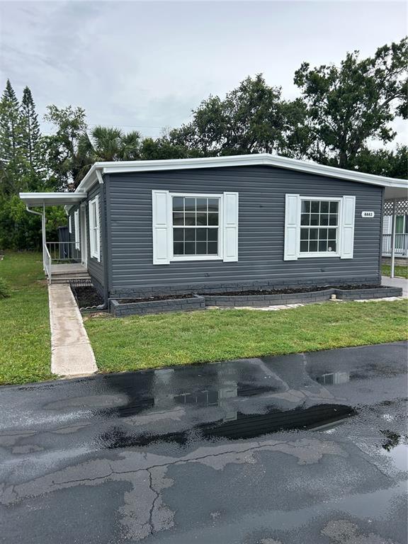 A gray manufactured home features white shutters, a concrete walkway, and a dark asphalt driveway — 4443 TUCKER SQUARE, NEW PORT RICHEY, FL