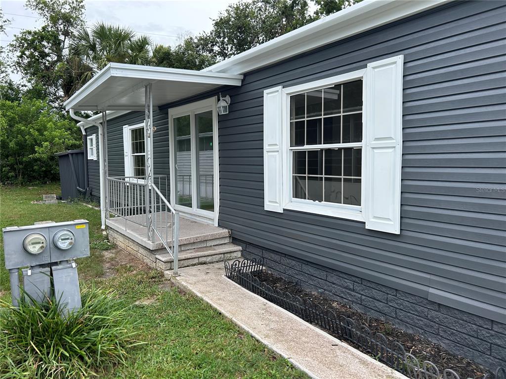 The exterior of a gray-sided mobile home features a small covered porch and sliding doors — 4443 TUCKER SQUARE, NEW PORT RICHEY, FL