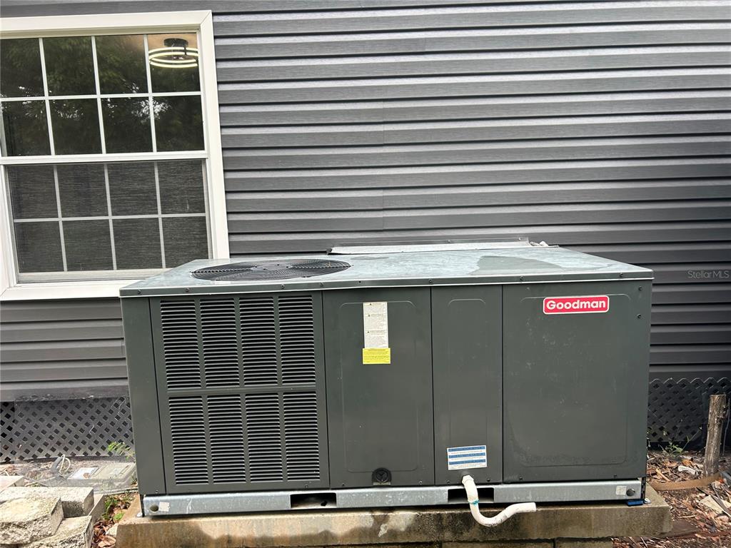 A Goodman HVAC unit sits on a concrete pad against gray vinyl house siding — 4443 TUCKER SQUARE, NEW PORT RICHEY, FL