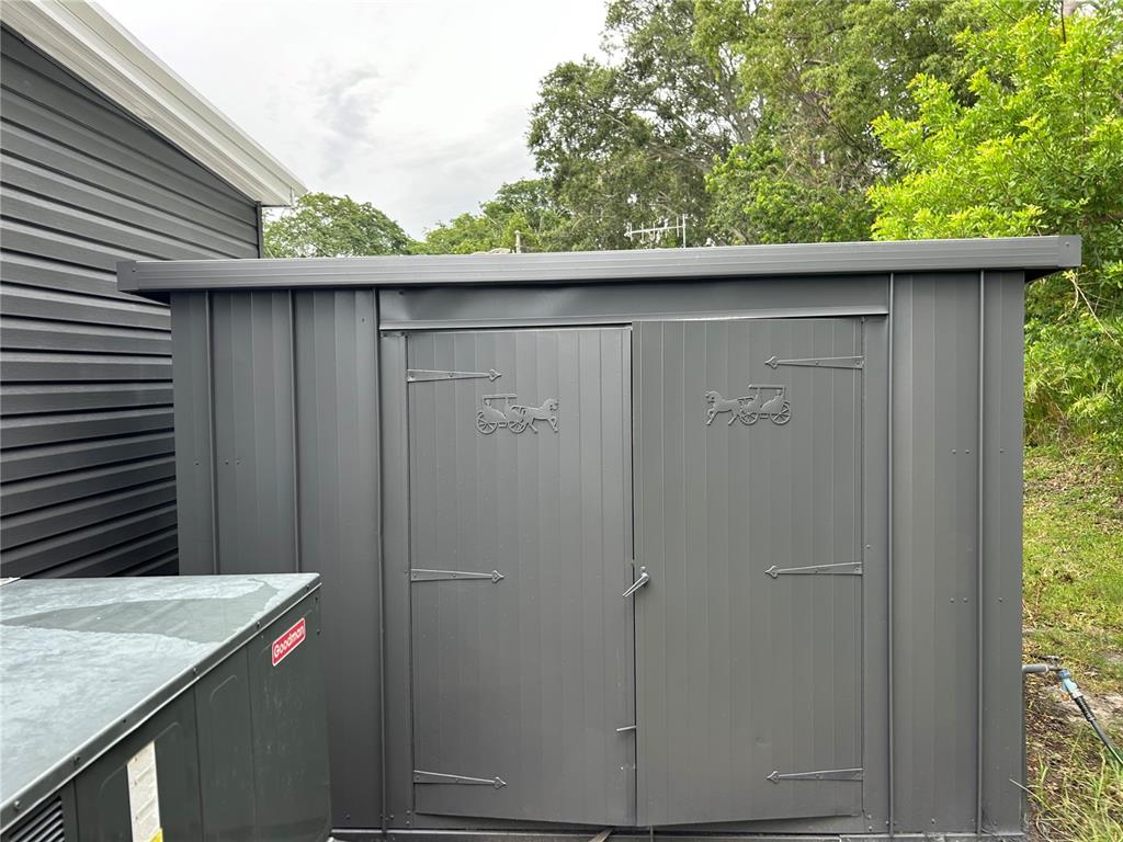 A dark gray metal storage shed stands next to a house and an air conditioning unit — 4443 TUCKER SQUARE, NEW PORT RICHEY, FL