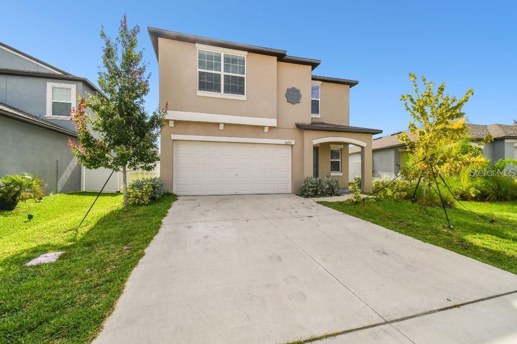 A two-story suburban house features a tan stucco exterior, a two-car garage, and a driveway — 6335 TEN ACRE COURT, ZEPHYRHILLS, FL