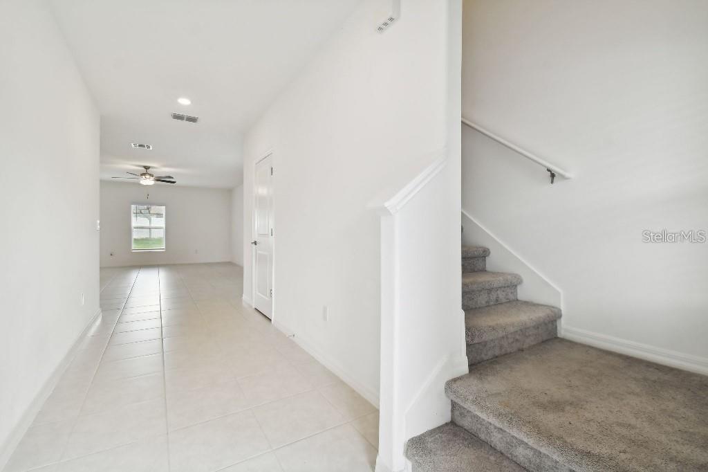 A hallway with tile flooring leads to a living area, with carpeted stairs on the right — 6335 TEN ACRE COURT, ZEPHYRHILLS, FL