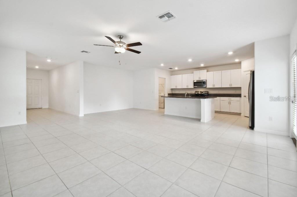 An open-concept kitchen and living area with white cabinets, a kitchen island, and tile flooring — 6335 TEN ACRE COURT, ZEPHYRHILLS, FL