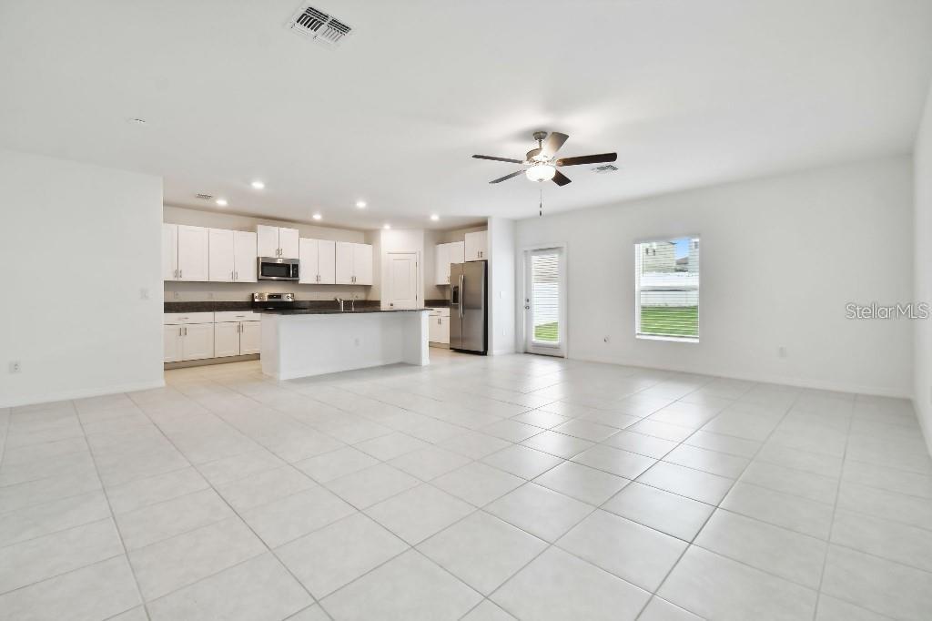 An open-concept kitchen and living area features white cabinets, tile flooring, and a ceiling fan — 6335 TEN ACRE COURT, ZEPHYRHILLS, FL