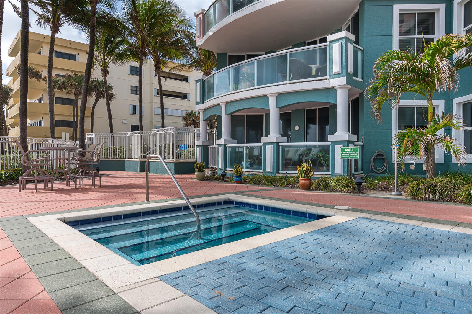 A hot tub sits on a paved patio next to a multi-story teal residential building — 2051 SE 3rd Street # 101, Deerfield Beach FL 33441, DEERFIELD BEACH, FL